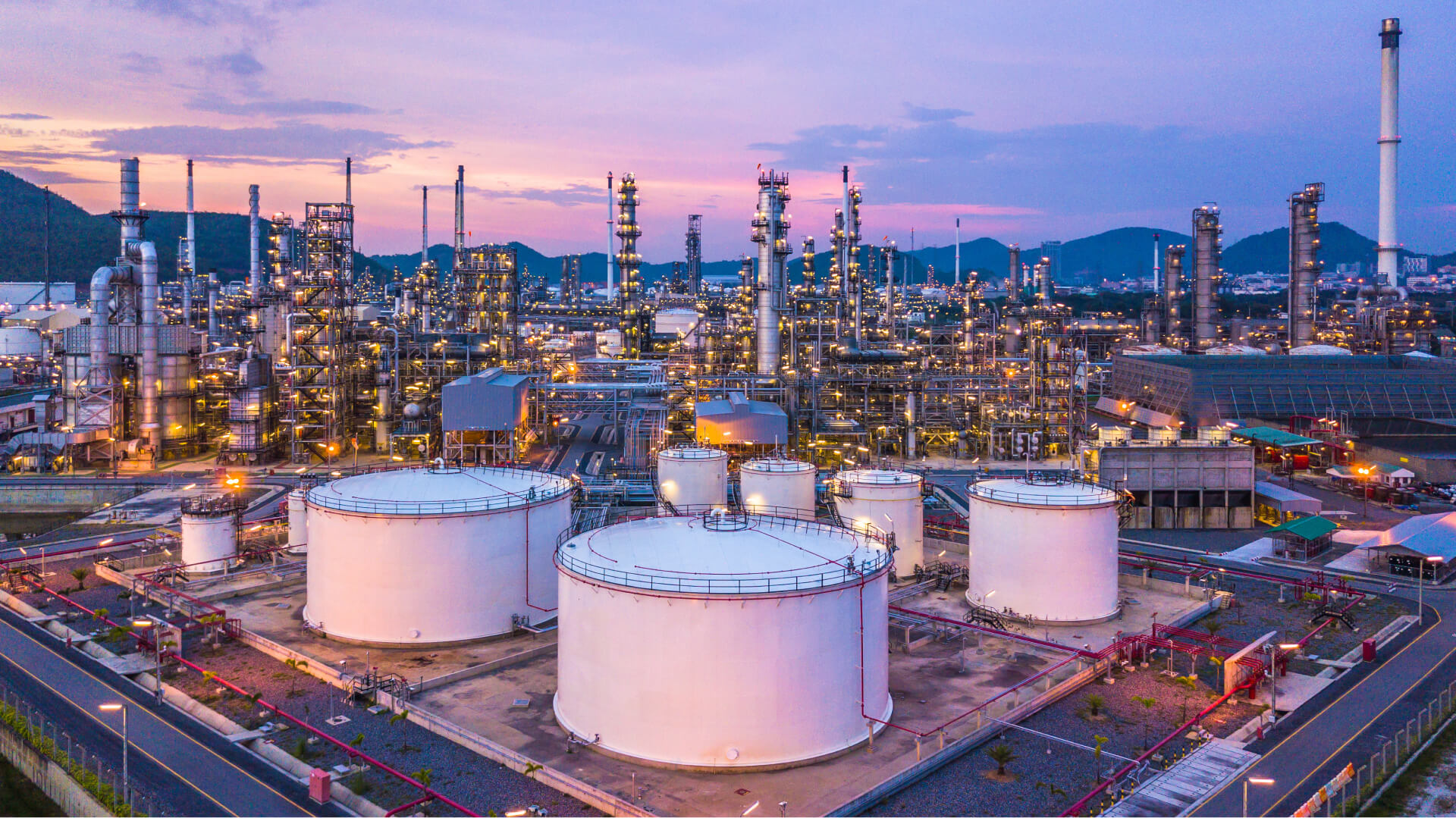 Aerial view of oil and gas chemical tanks with petrochemical processing plant background at twilight.