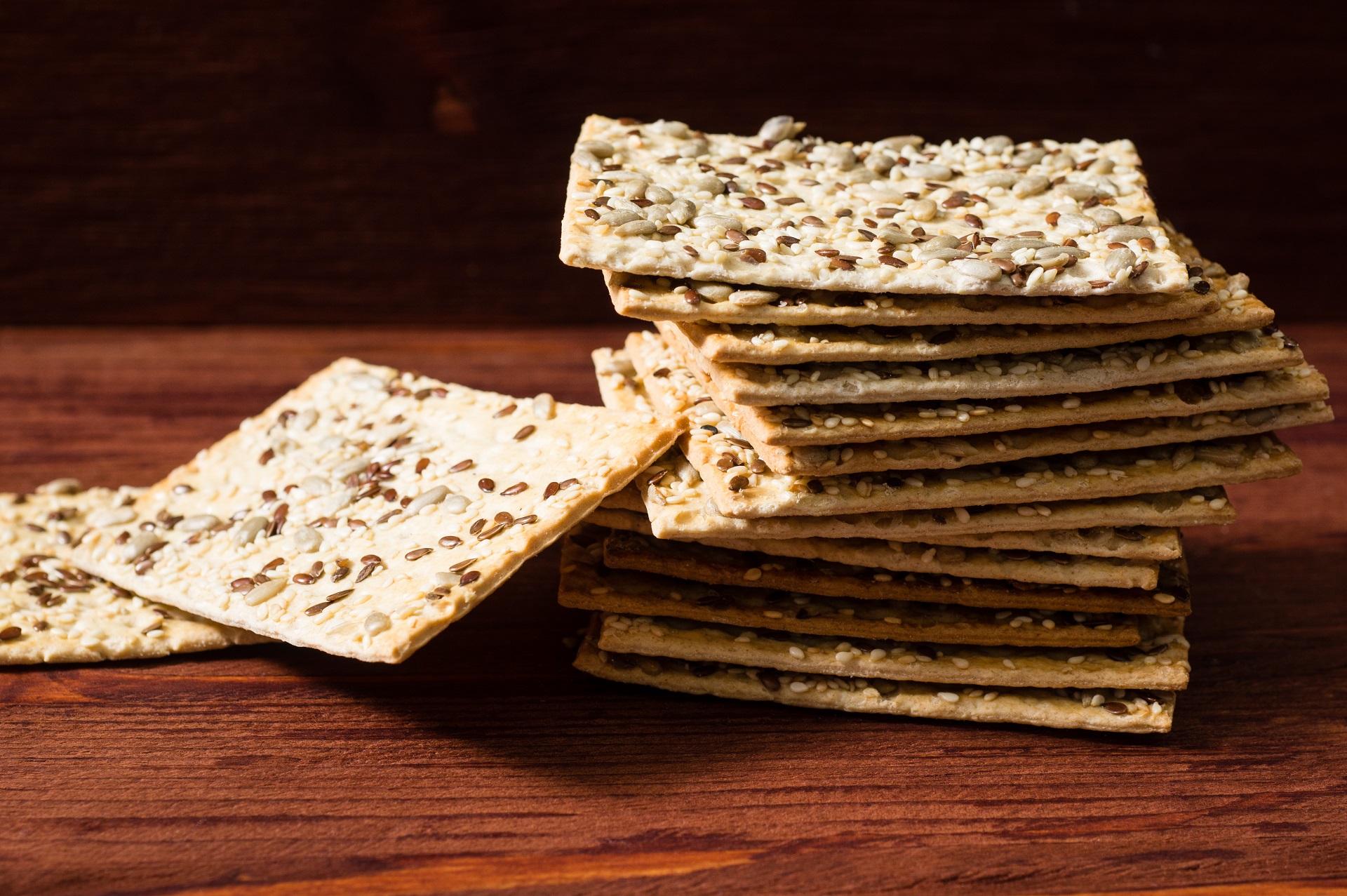 A stack of sesame seed flat bread crackers on a wooden table.