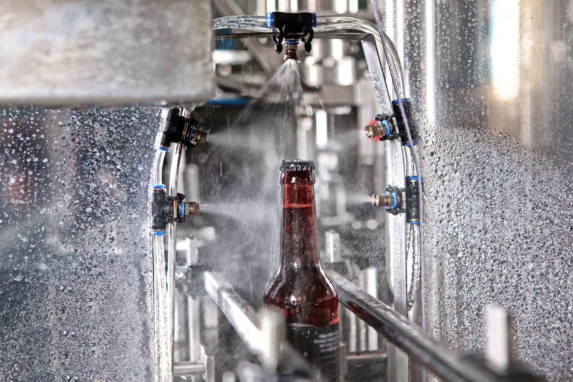 Detail of A bottle of beer on a conveyor belt under a stream of water. Only the bottle is in focus. The concept of production.