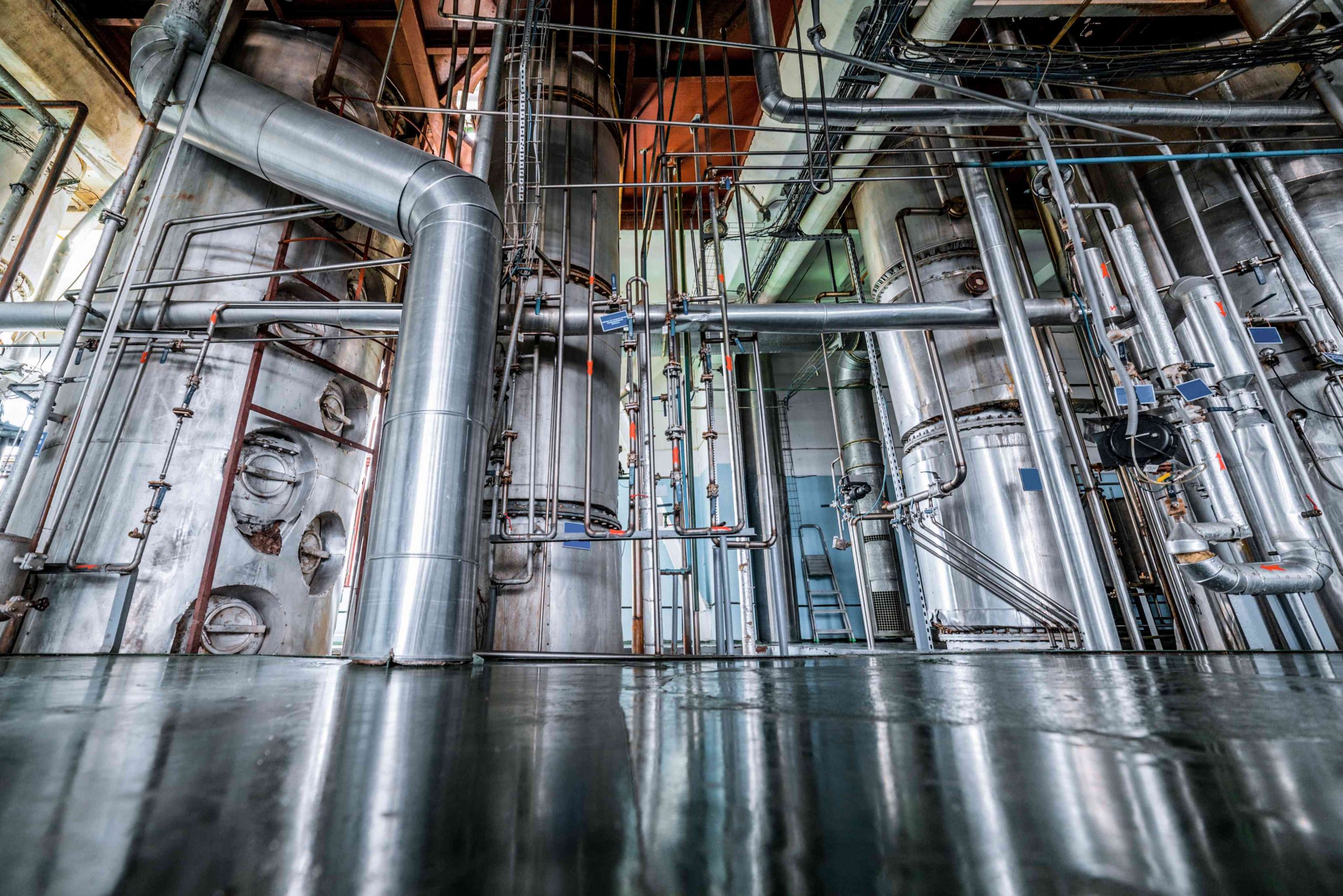 Silvery distillation columns at a chemical processing plant entangled in a multitude of pipes, valves, and sensors.